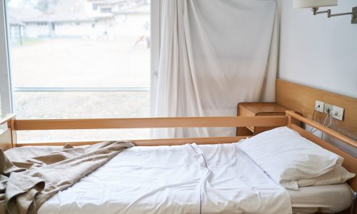 Interior of rehabilitation center with white sheet and pillow on empty bed in room