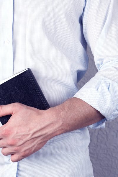 A man in a shirt holds a Bible book in his hands. Christian. On a gray background. Pastor. Prayer.