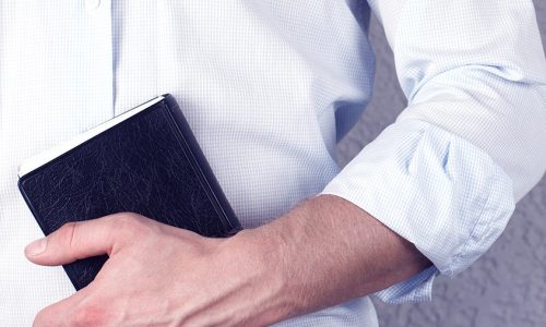 A man in a shirt holds a Bible book in his hands. Christian. On a gray background. Pastor. Prayer.