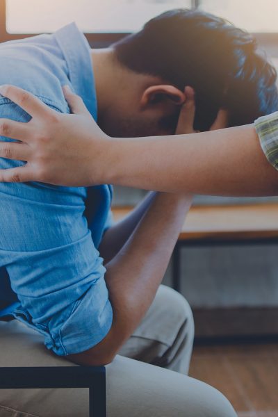 A Christian young man  praying for his friends while sitting on wooden chair at church prayer room to encourage and support him in his problem and spiritual growth.
