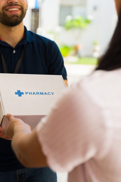 Smiling delivery man holding a white box with the word pharmacy on it while delivering medication to a woman